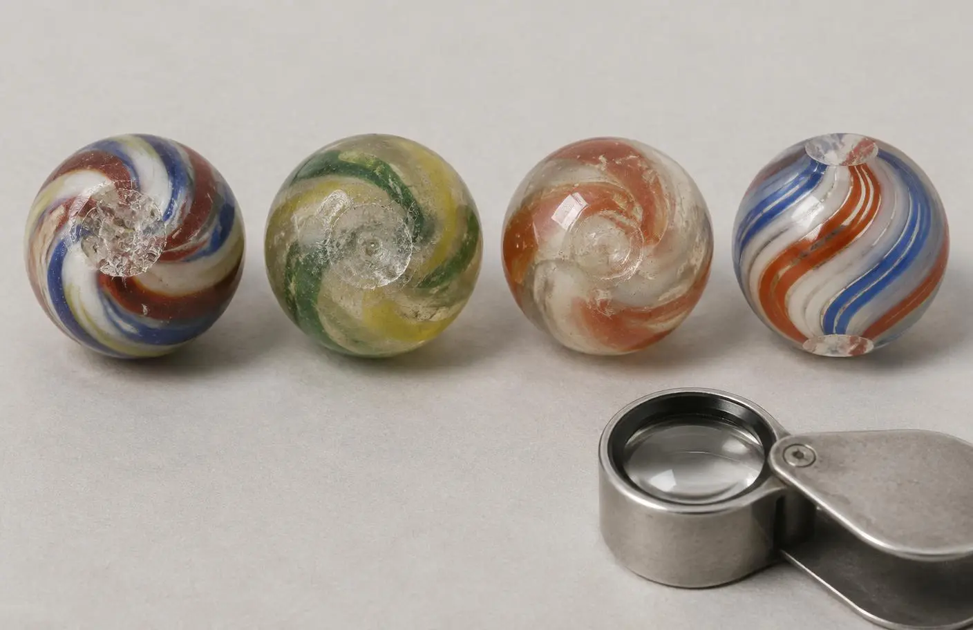 Four editorially reconstructed marbles displaying rough and ground pontils, transitional construction and machine cut-off marks