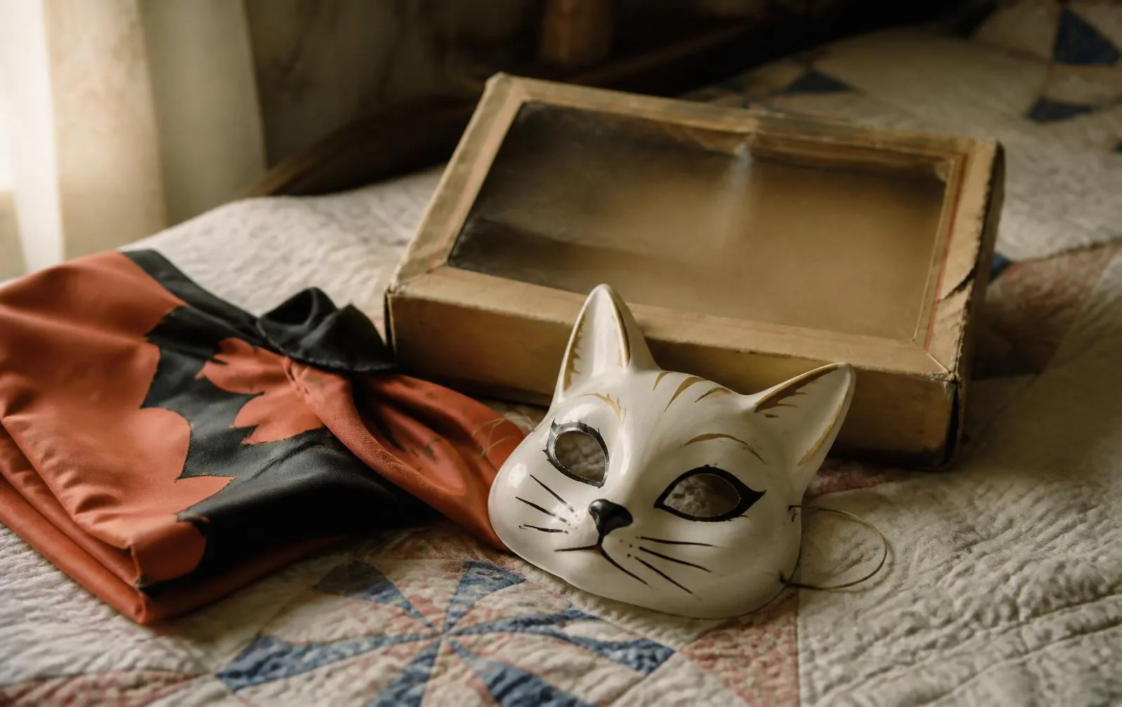 A vintage child's Halloween mask and printed cape beside an aged cardboard costume box with a cellophane window