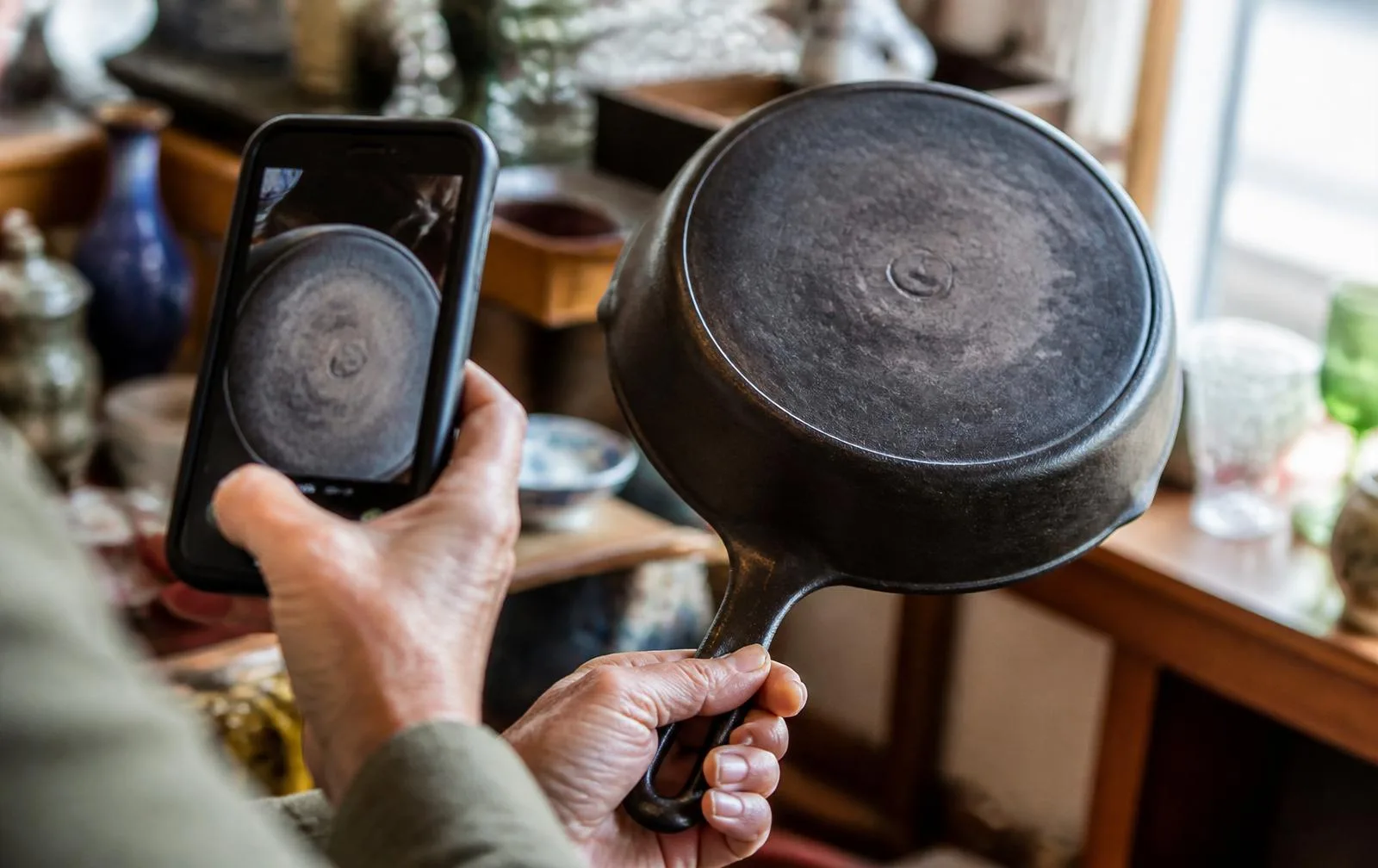 A shopper photographing the underside of a vintage cast iron skillet at an estate sale to research the maker's mark