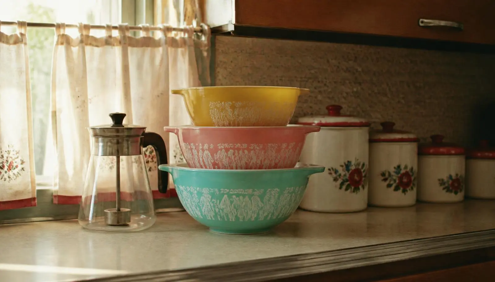Mid-century patterned opaque glass mixing bowls in turquoise, pink and yellow stacked on a vintage formica kitchen counter