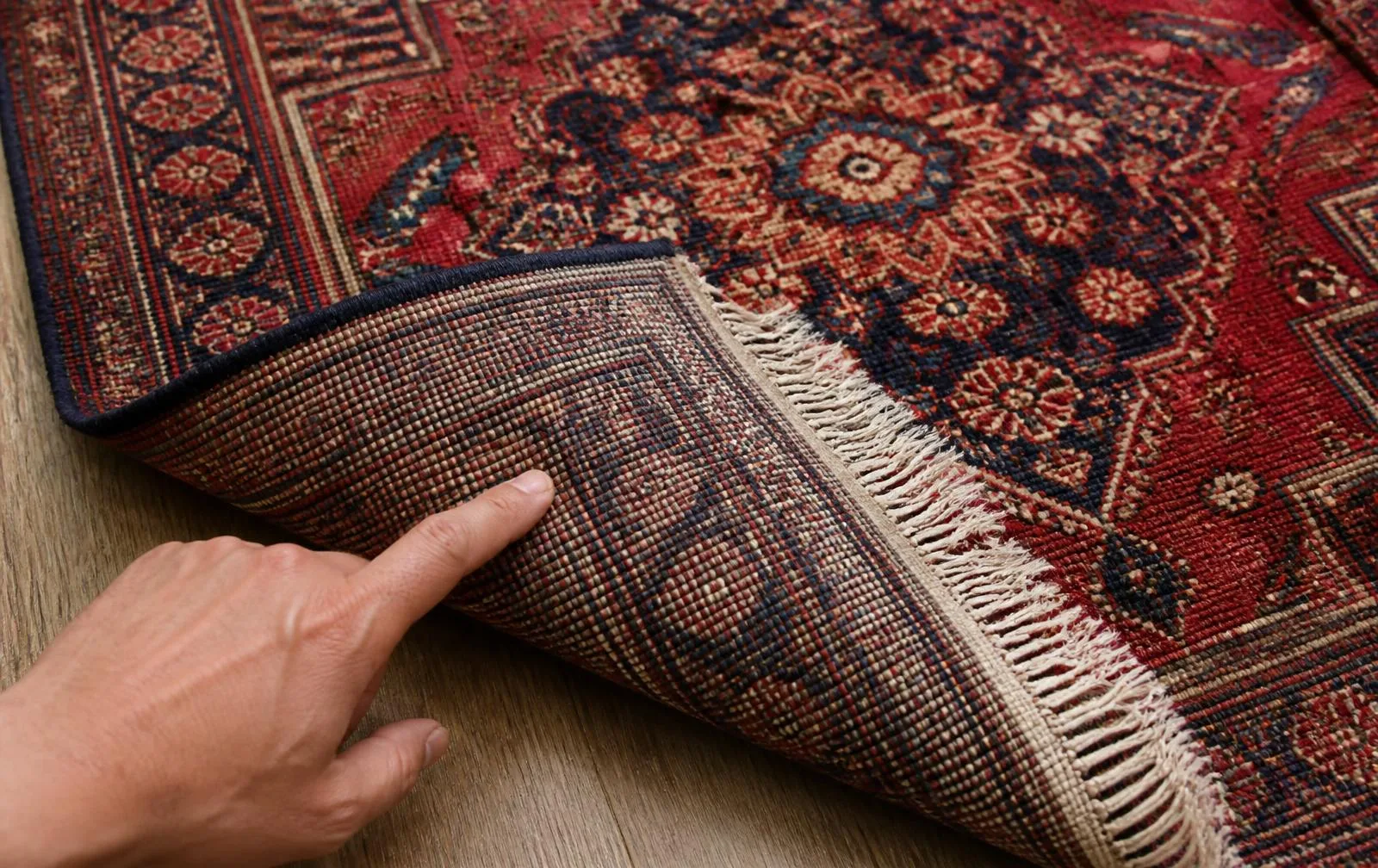 Hand-knotted Persian style rug folded back to show dense irregular knots on the reverse, with fringe emerging from the warp threads
