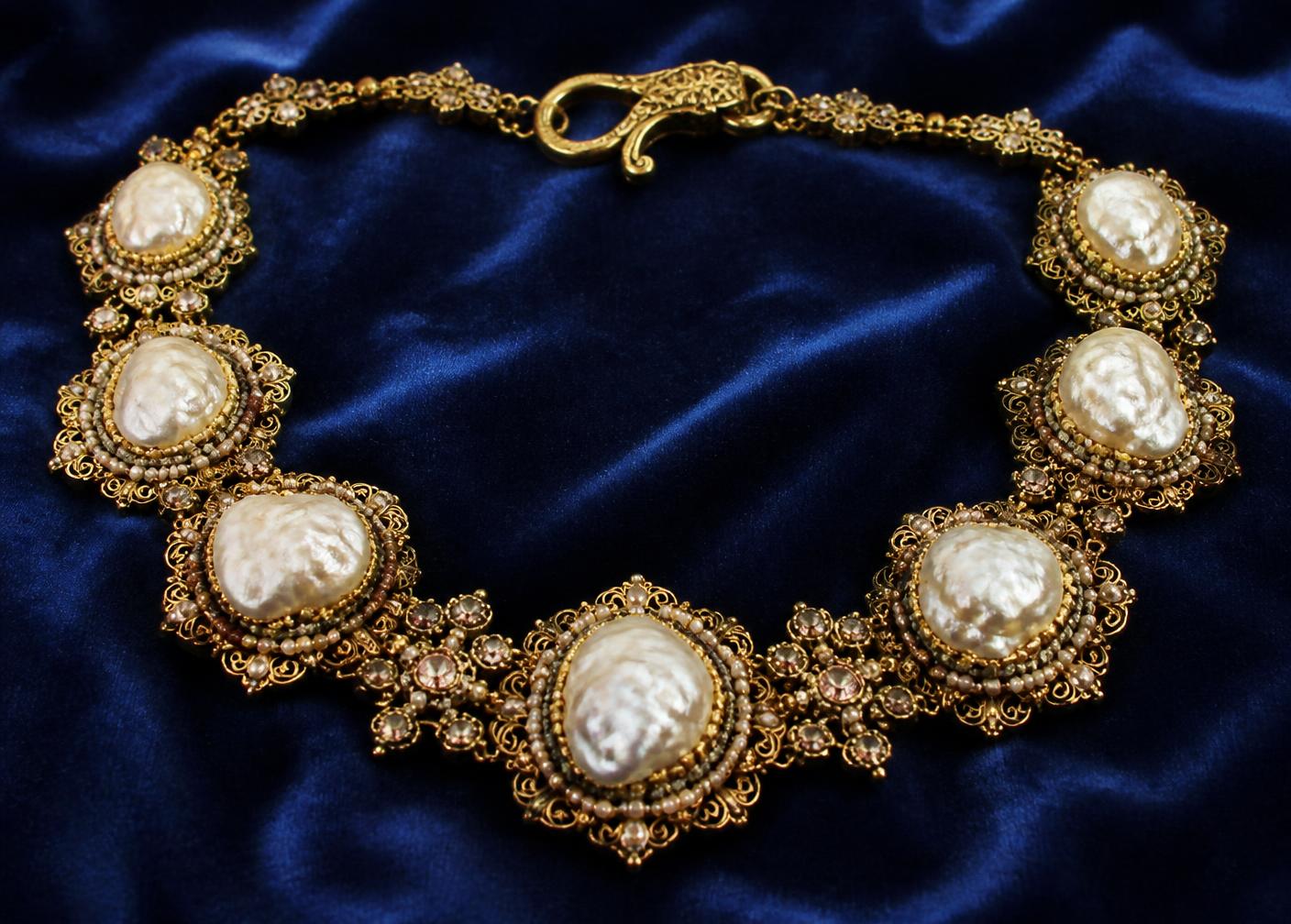 An elaborate hand-wired costume necklace on blue velvet: irregular baroque glass pearls on gilt filigree backplates with seed beads and small crystals, ornate filigree hook clasp
