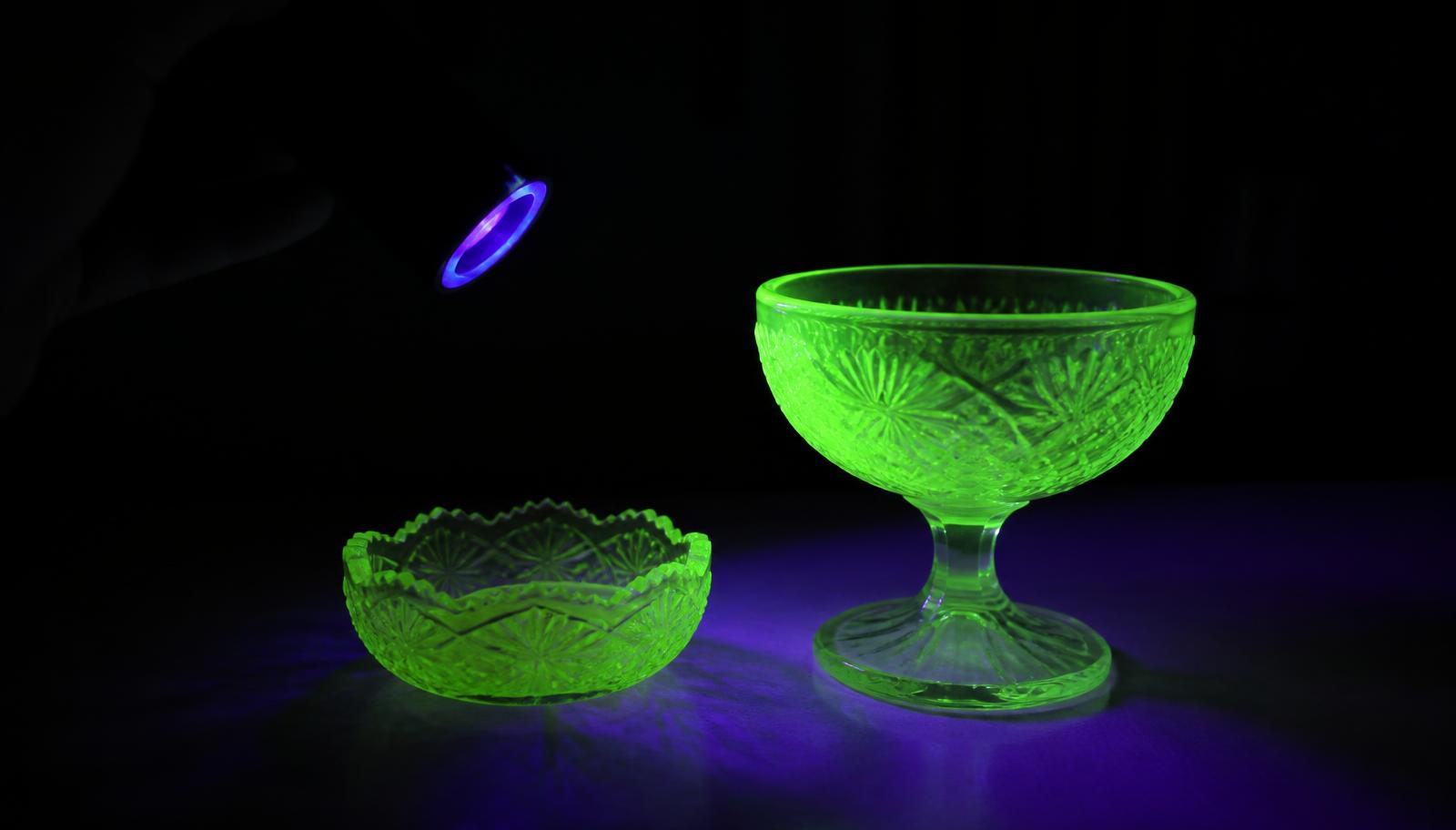 Two pieces of yellow-green pressed glass fluorescing bright electric green under a handheld UV blacklight in a dark room
