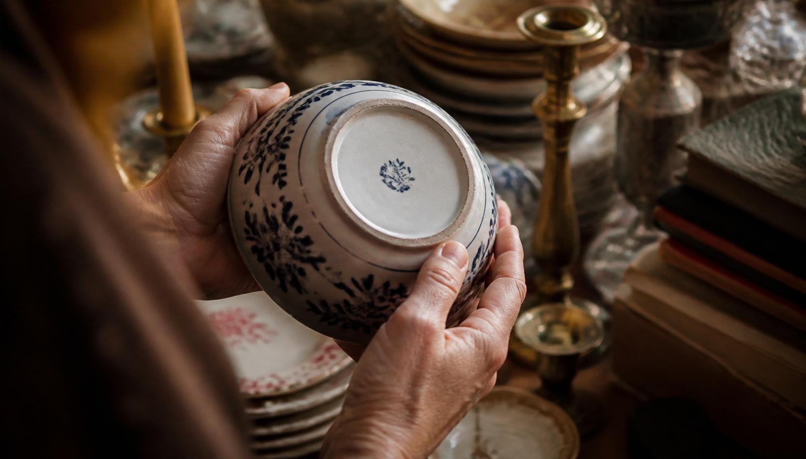Hands turning over a blue-and-white ceramic bowl to check the maker's mark