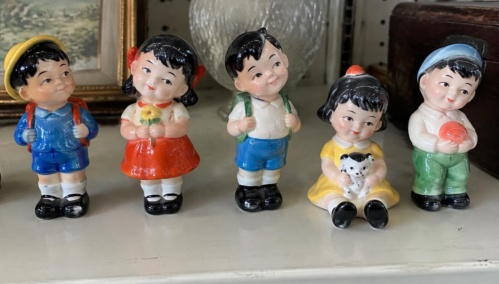 A row of glossy brightly painted Japanese porcelain child figurines on a thrift store shelf