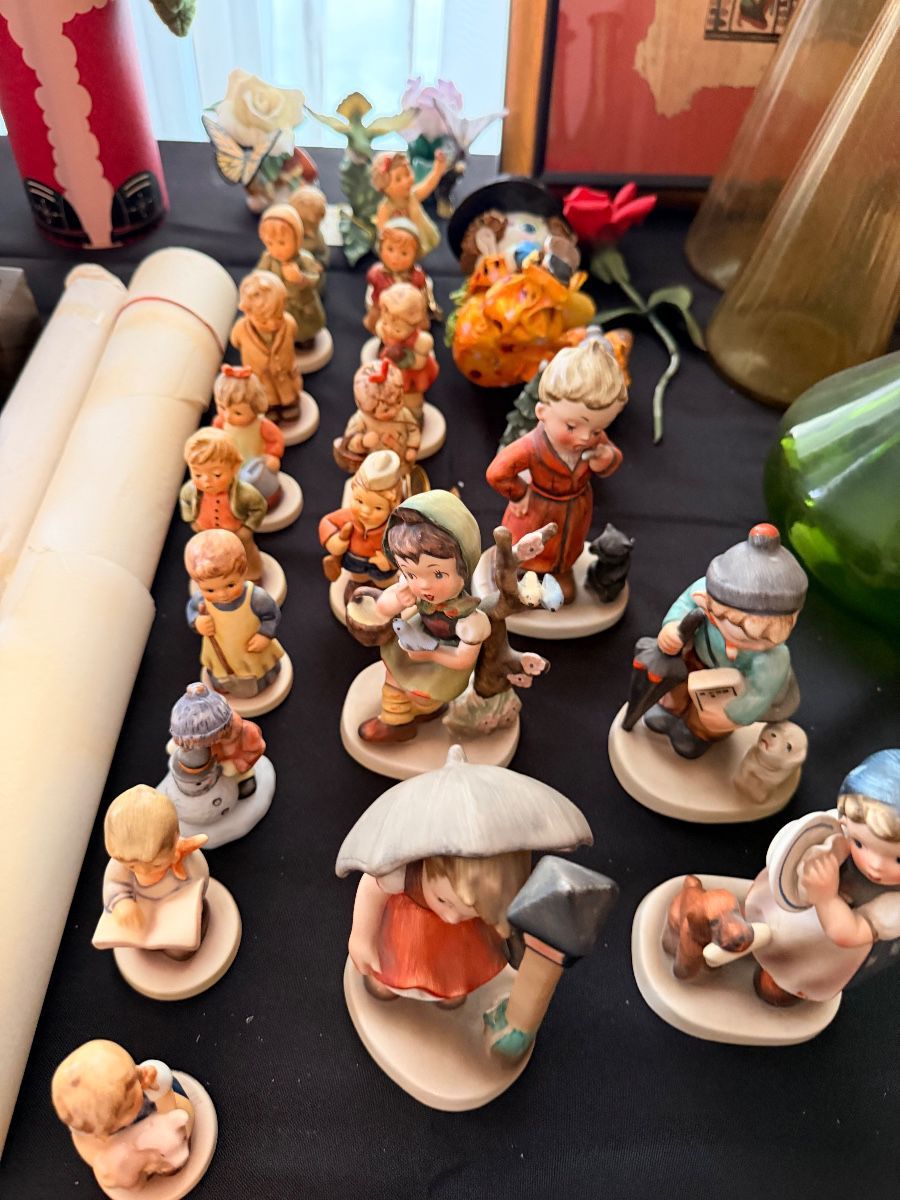 A large collection of hand-painted Hummel-style porcelain figurines arranged on a table at the Laguna Hills estate sale