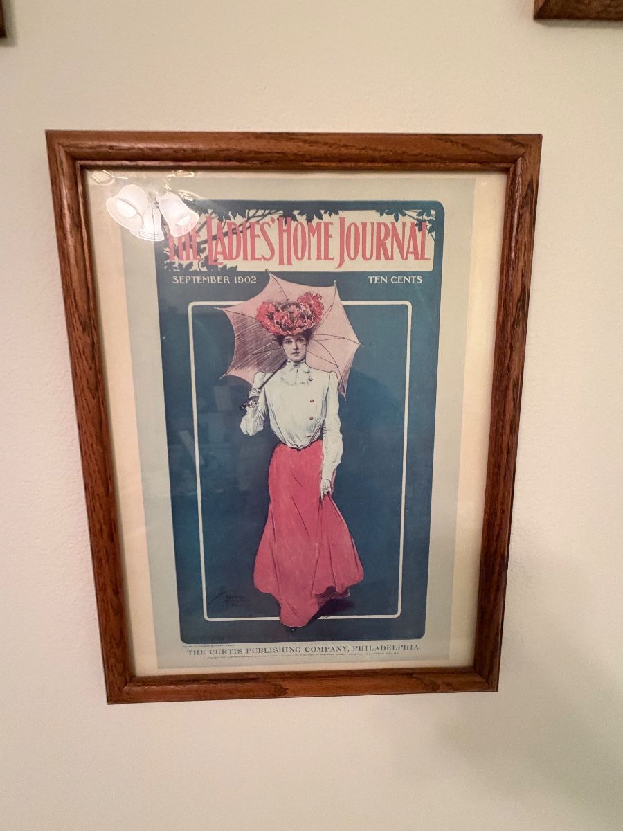 A framed original Ladies' Home Journal magazine cover from September 1902 showing a woman with a parasol in a red skirt