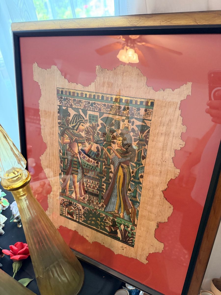 A framed Egyptian papyrus painting depicting figures in traditional dress, matted in red