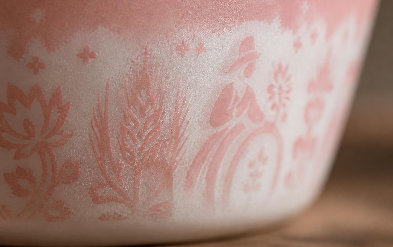 Extreme close-up of a pink and white vintage Pyrex surface showing chalky etched haze where the glossy enamel print has eroded and softened.