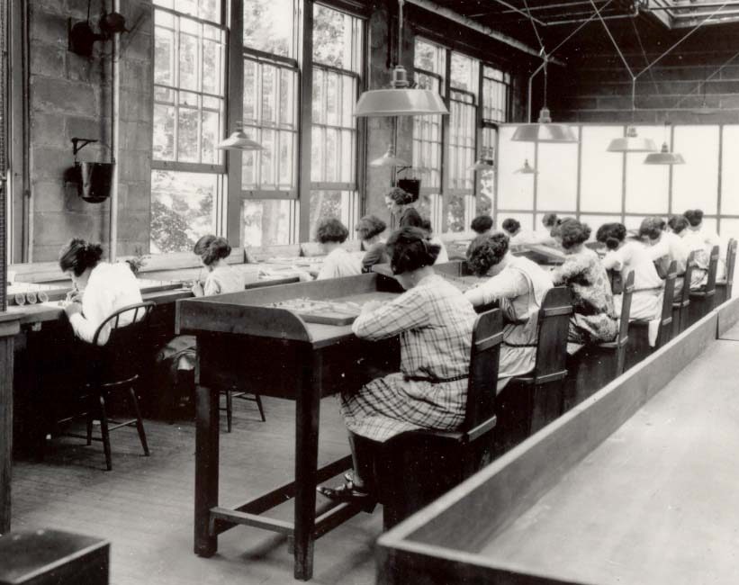 Rows of young women in a 1920s dial-painting studio applying radium luminous paint to watch faces with no protective equipment