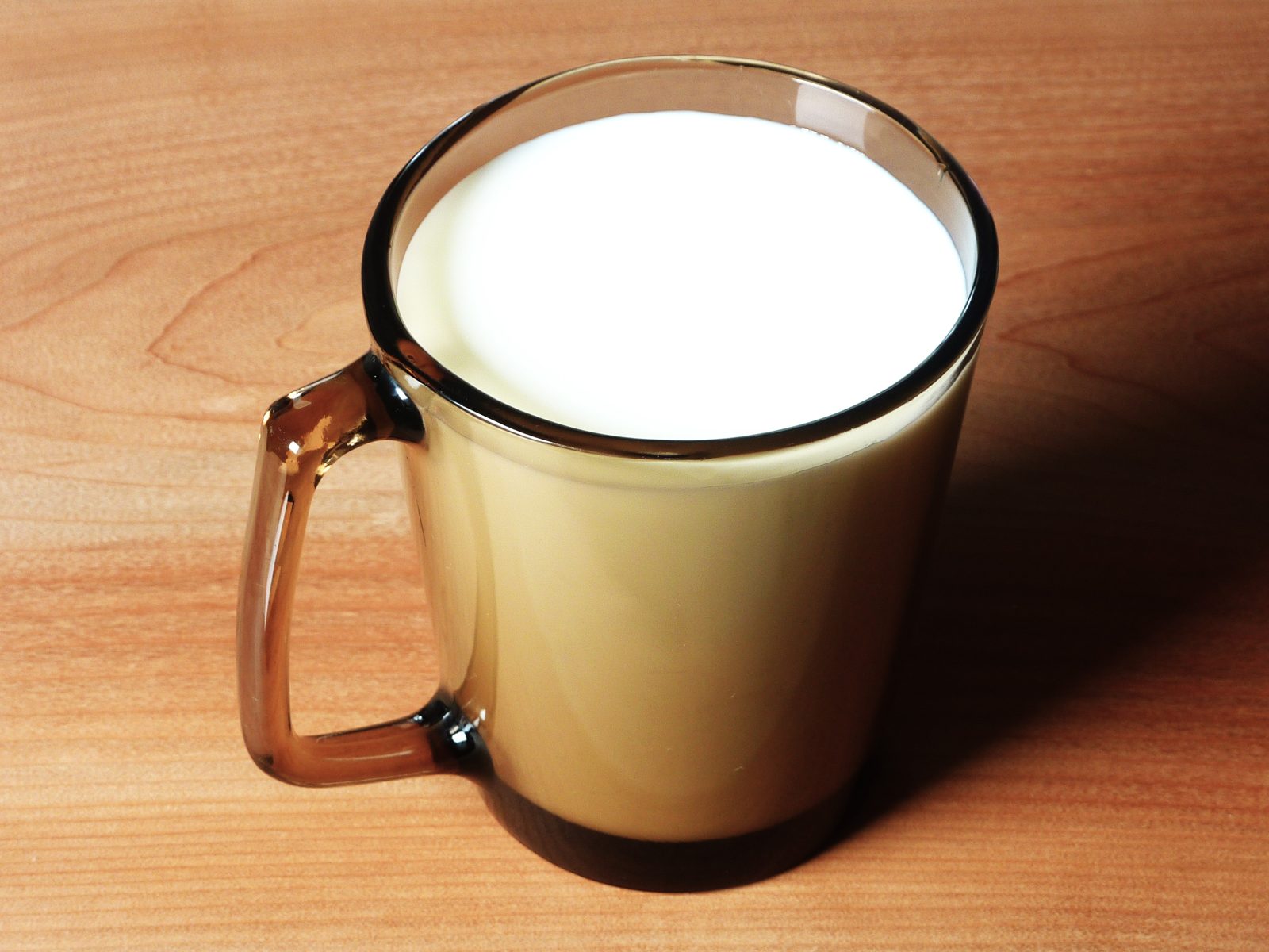 A smoked-amber vintage Pyrex Fireside glass mug filled with milk, glowing warm on a wooden table.